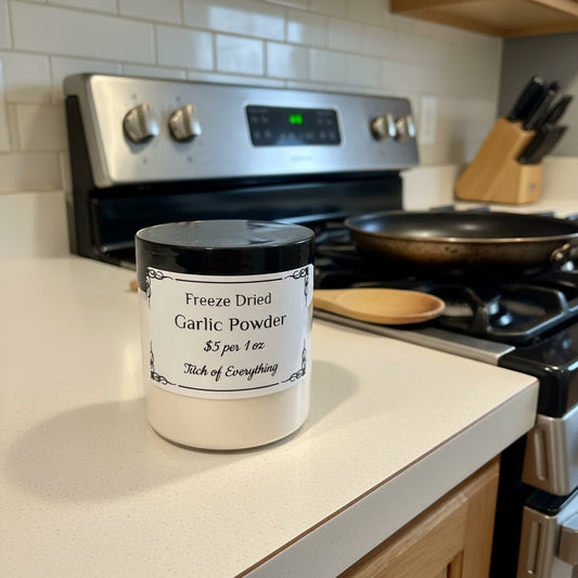 Titch of Everything freeze dried garlic powder in a white jar on a kitchen counter next to a stove and skillet.